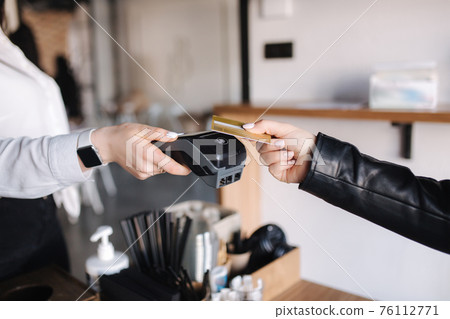 Female customer making wireless or contactless payment using credit card. Closeup of human hands during payment. Store worker accepting payment over nfc technology. Side view 76112771