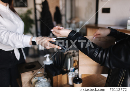 Female customer making wireless or contactless payment using smartwatch. Closeup of hands during payment. Store worker accepting payment over nfc technology Female customer making wireless or contactless payment using smartwatch. Closeup of hands during payment. Store worker accepting payment over nfc technology 76112772
