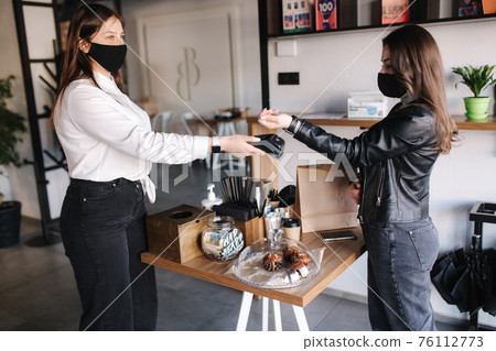 Female customer making wireless or contactless payment using smartwatch. Store worker accepting payment over nfc technology Female customer making wireless or contactless payment using smartwatch. Store worker accepting payment over nfc technology 76112773