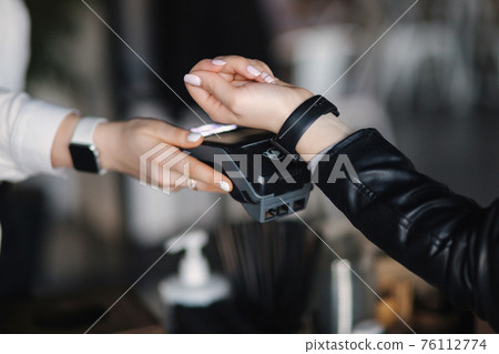 Female customer making wireless or contactless payment using smartwatch. Closeup of hands during payment. Store worker accepting payment over nfc technology Female customer making wireless or contactless payment using smartwatch. Closeup of hands during payment. Store worker accepting payment over nfc technology 76112774