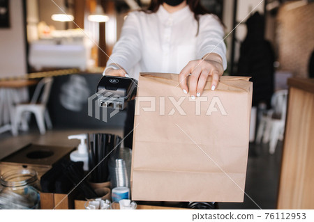 Cashier hand holding credit card reader machine and package with food. Contactless payments concept. Middle celection. Closeup 76112953