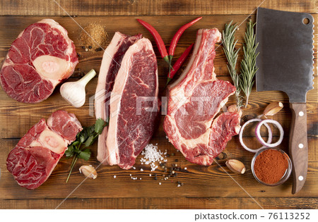 Pieces of raw meat on a wooden table. Pepper, garlic, spices.Knife. Top view. 76113252
