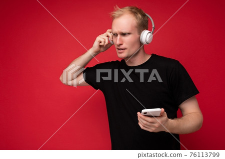 Thoughtful handsome young man isolated over background wall wearing everyday clothes holding and 76113799