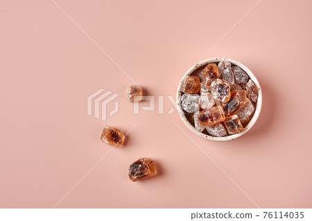 Brown caramelized lump cane sugar cubes in a bowl on pink powdered background Brown caramelized lump cane sugar cubes in a bowl on pink powdered background 76114035