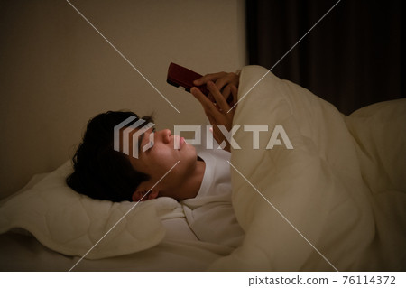 Image of a young man looking at a smartphone with a futon and a man staying up late 76114372