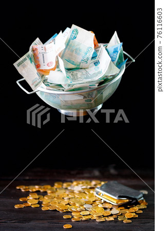 Russian money in a sieve on a dark background. The concept of financial inequality. Russian money in a sieve on a dark background. The concept of financial inequality. 76116603