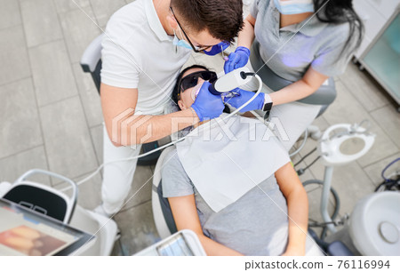Doctor and assistant examining patient teeth with intraoral scanner. Doctor and assistant examining patient teeth with intraoral scanner. 76116994