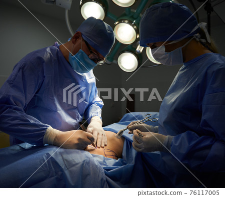 Surgeon and assistant doing plastic surgery in operating room. Surgeon and assistant doing plastic surgery in operating room. 76117005
