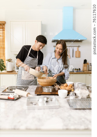 Asian couple Help each other to make a bakery In a romantic atmosphere in the kitchen at home. Young people work together to mix the ingredients in a wooden bowl before stirring them together. Asian couple Help each other to make a bakery In a romantic atmosphere in the kitchen at home. Young people work together to mix the ingredients in a wooden bowl before stirring them together. 76117610