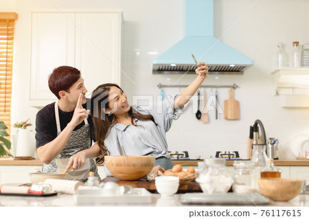 A couple uses their smart phone to take a picture while admiring his wife's cooking work With a happy face in an atmosphere of love 76117615