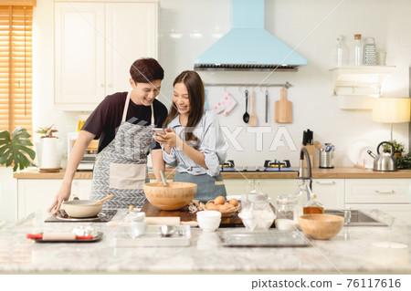 A couple uses their smart phone to take a picture while admiring his wife's cooking work With a happy face in an atmosphere of love A couple uses their smart phone to take a picture while admiring his wife's cooking work With a happy face in an atmosphere of love 76117616