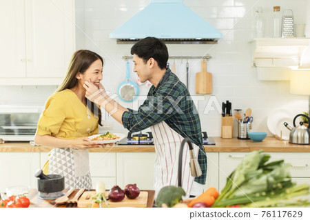 Portrait young couple in love helping to cook In a romantic atmosphere at home and looking at camera with smile face. 76117629
