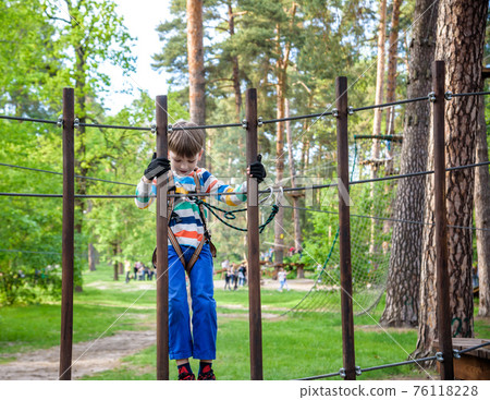 Cute boy enjoying a sunny day in a climbing adventure activity park. shadows from a rope 76118228