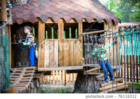 Two little boys playing together and having fun. Lifestyle family moment of siblings on playground. Kids friends play on tree house climbing on rope or stairs Two little boys playing together and having fun. Lifestyle family moment of siblings on playground. Kids friends play on tree house climbing on rope or stairs 76118312