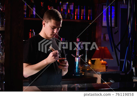 Barman fills black burnt ceramic bowl for hookah smoking different types of tobacco. Barman fills black burnt ceramic bowl for hookah smoking different types of tobacco. 76119858