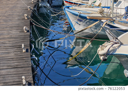 Motorboats moored to brown wooden pier bollards with ropes 76122053