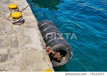 Large old tires of black colour hang on concrete pier edge to protect boats from impact 76122057