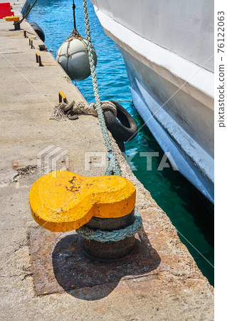 Yellow mooring bollard with rope on grey concrete pier Yellow mooring bollard with rope on grey concrete pier 76122063