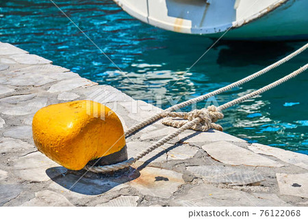 Yellow mooring bollard with rope on grey concrete pier Yellow mooring bollard with rope on grey concrete pier 76122068