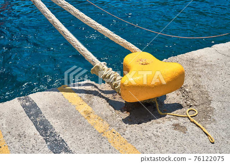 Yellow mooring bollard with rope on grey concrete pier Yellow mooring bollard with rope on grey concrete pier 76122075
