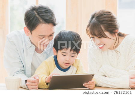 A young family sitting at a living room table and looking at a tablet A young family sitting at a living room table and looking at a tablet 76122161
