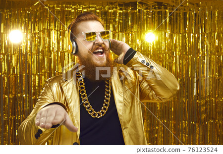 Happy DJ in shiny jacket, headphones and cool sunglasses playing music at disco party Happy DJ in shiny jacket, headphones and cool sunglasses playing music at disco party 76123524