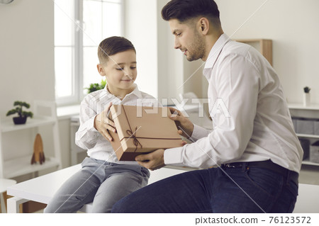 Happy little son giving a box with a birthday or Father's Day present to his dad Happy little son giving a box with a birthday or Father's Day present to his dad 76123572