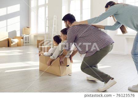 Rear view on overjoyed parents riding kids in cardboard box on moving day Rear view on overjoyed parents riding kids in cardboard box on moving day 76123576