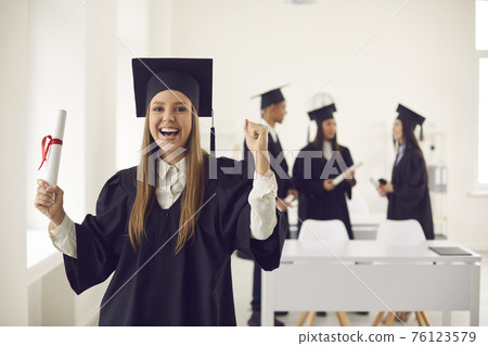 Excited student holding her diploma and celebrating college or university graduation 76123579
