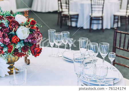 Fancy table set for dinner with flower composition in restaurant, luxury interior background. Wedding elegant banquet decoration and items for food arranged by catering service on white table. 76124174