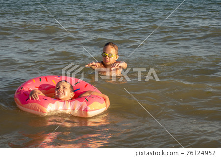 Two brothers 5 and 10 years old swim and have fun in the sea on a clear sunny day. 76124952