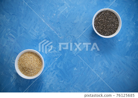 Quinoa and chia seeds are organic food for a healthy diet. In a round bowl. Two white cups. The blue texture is painted with blue oil paints 76125685