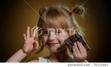 Portrait of teen smiling child kid girl with milk chocolate bar showing thumb up gesture, ok sign Portrait of teen smiling child kid girl with milk chocolate bar showing thumb up gesture, ok sign 76125807