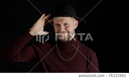 Facial expression of handsome man in stylish hat looking at camera and smiling on black background Facial expression of handsome man in stylish hat looking at camera and smiling on black background 76125982