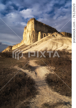 Beautiful white mountain peak lit by sun. White clouds and blue sky on background. Epic rock formation 76126020