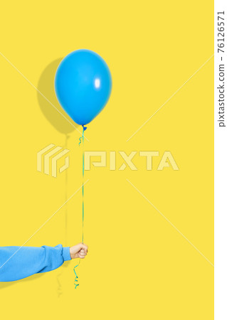 Female hand hold blue balloon. Party or present concept. Blue Balloon and hand in blue hoodie isolated on yellow backgroun Female hand hold blue balloon. Party or present concept. Blue Balloon and hand in blue hoodie isolated on yellow backgroun 76126571