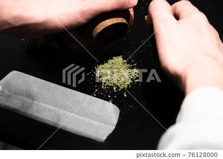 Cannabis in a grinder and other smoking utensils on a table 76128000