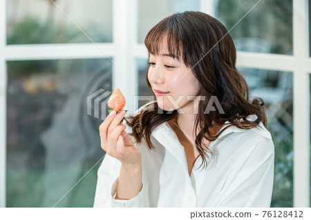 Woman holding a strawberry on the terrace 76128412