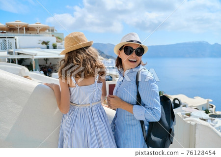 Tourists mom and daughter walking around the famous Greek island of Santorini Tourists mom and daughter walking around the famous Greek island of Santorini 76128454