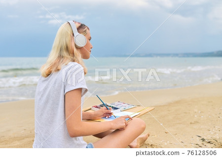 Young woman artist painting with watercolors sitting on the seashore Young woman artist painting with watercolors sitting on the seashore 76128506