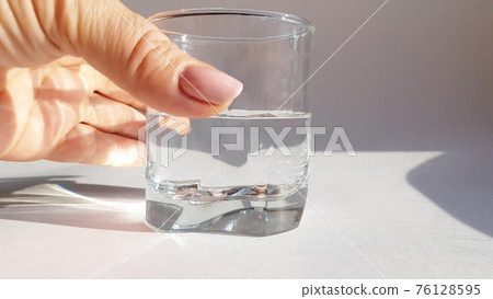 Close-up of female hand holding transparent glass with cold water on white background Close-up of female hand holding transparent glass with cold water on white background 76128595