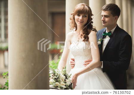 Lovely happy wedding couple, bride with long white dress posing in beautiful city Lovely happy wedding couple, bride with long white dress posing in beautiful city 76130702