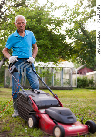 Positive elderly man with lawnmower when mowing the lawn Positive elderly man with lawnmower when mowing the lawn 76135598