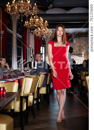 Attractive young woman in red dress walks through hall of a fashionable restaurant Attractive young woman in red dress walks through hall of a fashionable restaurant 76135600
