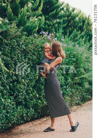 a small child sits on the mother's hands. momy's daughter is on vacation. tropical leaves. Travel to hot countries 76135706