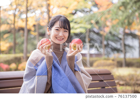 Woman eating an apple in an autumn park 76137500