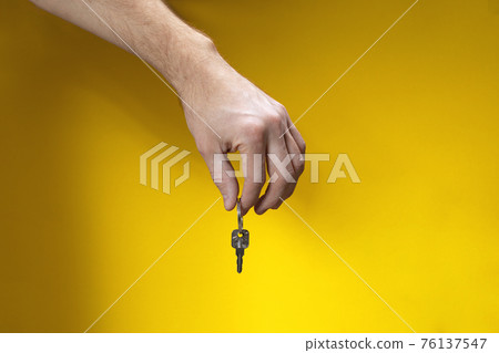 Man hand with key on yellow background with shadow. Solution is found. 76137547