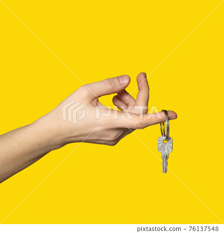 On finger of woman hand hangs key on bright yellow background. 76137548