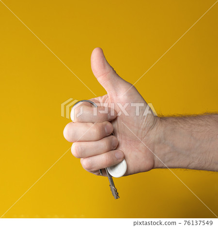 man hand holding house keys on yellow background. makes thumbs up gesture 76137549