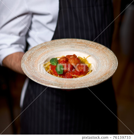 Chef hand holding tasty Italian pasta dish 76139733